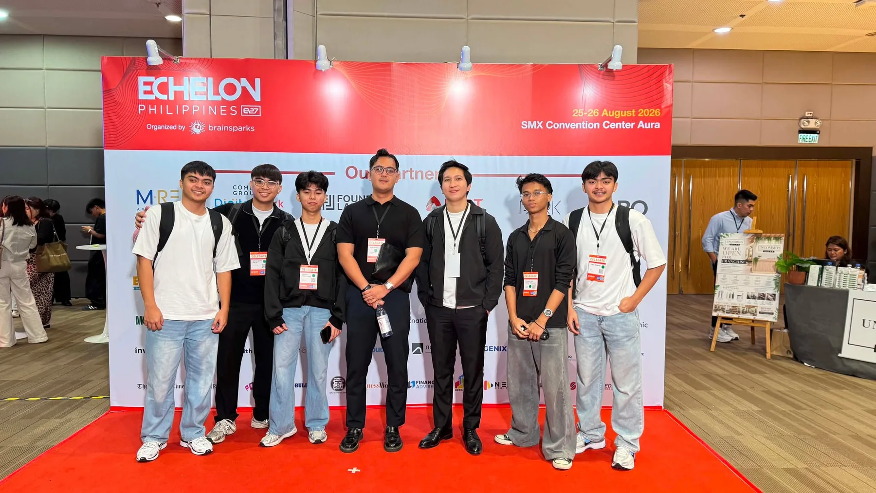 Seven Theoraux team members wearing delegate badges in front of the Echelon Philippines backdrop at SMX Convention Center Aura, August 25 to 26, 2026